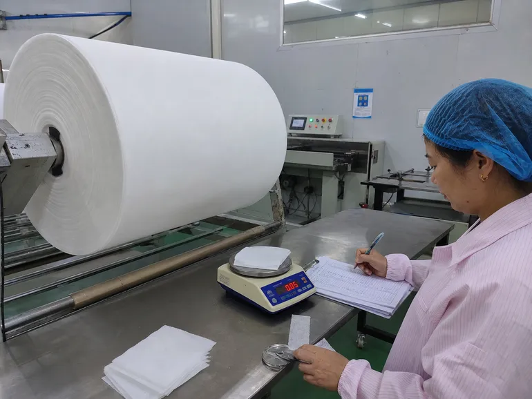 Spunbond polypropylene fabric roll undergoing basis weight inspection before cap production