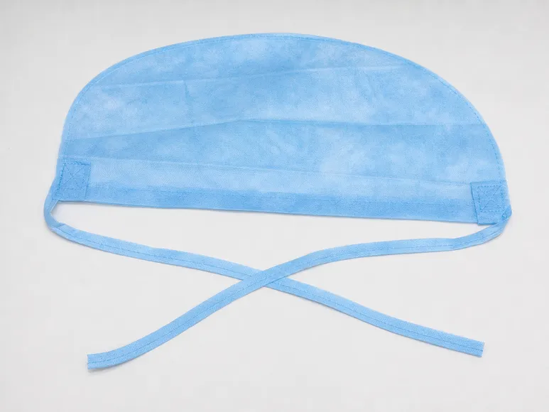 Surgical medical cap flat lay showing tie-back strings, spunbond polypropylene fabric texture, and reinforced attachment points